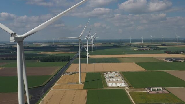 Aerial view of wind turbines standing in agricultural fields with green and golden crops under a blue sky in Dronten, Flevoland, Netherlands.