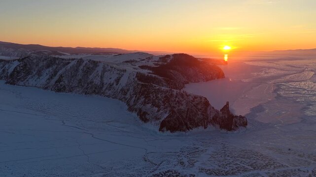 Aerial view of Lake Baikal with snow-covered cliffs and frozen ice during golden hour in Khuzhir, Irkutsk Oblast, Russia.