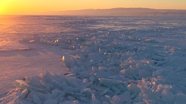 Aerial view of Lake Baikal featuring jagged ice formations glowing under the golden sunset light in Khuzhir, Irkutsk Oblast, Russia.