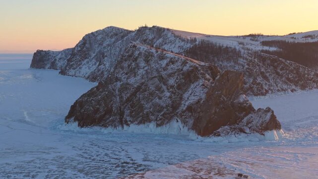 Aerial view of the rocky cliffs of Lake Baikal covered in snow during golden hour in Khuzhir, Irkutsk Oblast, Russia.