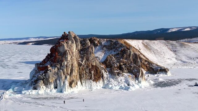 Aerial view of Shamanka Rock on frozen Lake Baikal with hovercrafts and people on the ice in Khuzhir, Irkutsk Oblast, Russia.