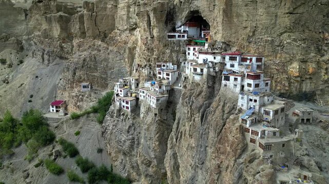 Aerial view of Phukthal Gompa, a historic Buddhist monastery built into a cliffside, with white buildings and rocky terrain in Phugtal, Himachal Pradesh, India.