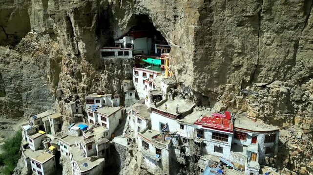 Aerial view of Phukthal Gompa monastery built into a sheer cliff face with white buildings and red roofs in Phugtal, Himachal Pradesh, India.