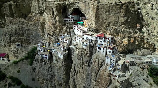 Aerial view of Phukthal Gompa monastery built into a cliffside cave with white buildings and rugged rock formations in Phugtal, Himachal Pradesh, India.