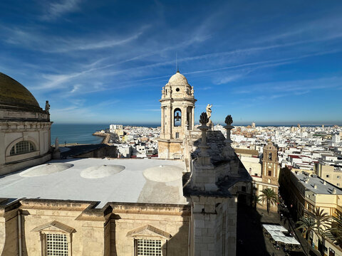 View of the historic Cadiz Cathedral with its iconic dome and bell tower overlooking the white rooftops of the city and the Atlantic Ocean in Cadiz, Andalusia, Spain.
