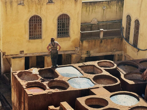 Fes, Morocco - 24 February 2026: View of a worker at the historic Chouara Tannery, surrounded by colorful dye vats and traditional ochre-colored buildings.