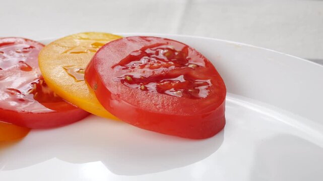 Chef arranges fresh yellow and red tomato slices on a white plate. Close-up of healthy gourmet salad preparation and bright organic vegetable layout for restaurant food styling.