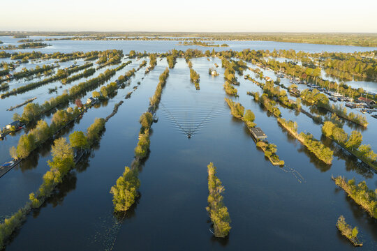 Aerial view of Scheendijk in Breukelen featuring narrow tree-lined islands and waterways with a small boat creating ripples in the water, Breukelen, Utrecht, Netherlands.