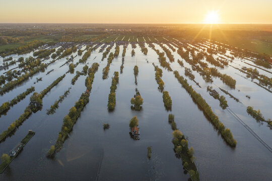 Aerial view of Scheendijk featuring narrow strips of land and trees surrounded by water at sunset, with golden light reflecting on the surface in Breukelen, Utrecht, Netherlands.