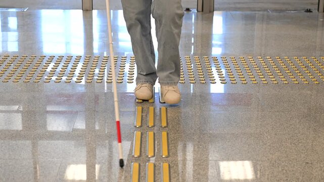 A blind woman walks on tactile paving. Close-up of her feet and a walking stick.