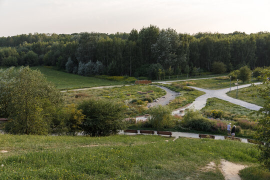 Active senior couple walking outdoors on a grassy hill during day in summer park. Older man and woman spending time in nature. Kabaty, Park Cichociemnych, Gorka Kazoora, Warsaw, Masovian, Poland.