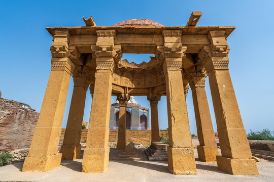 View of the historic stone pavilion at the Makli Necropolis with intricate carvings and columns under a clear blue sky in Thatta, Sindh, Pakistan.