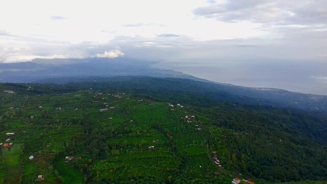 Aerial view of lush green hills, terraced fields, and coastal scenery near Singaraja in Kecamatan Buleleng, Bali, Indonesia.