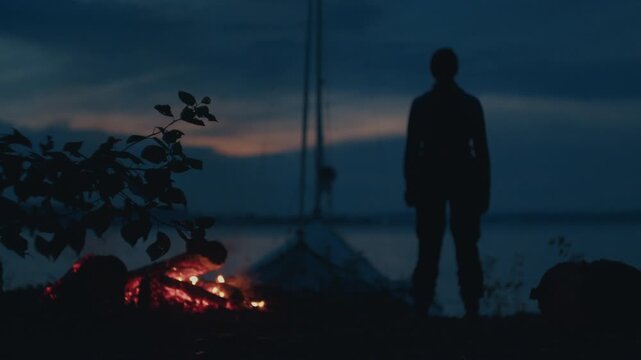 Sailing and camping in the wild. Woman sailor walks on the wild area with sailing boat on the background and bonfire on the foreground