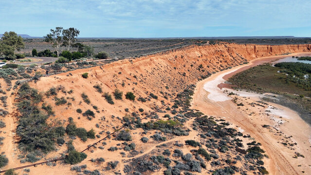 Aerial view of the red cliffs at Matthew Flinders Red Cliff Lookout, featuring rugged orange earth, sparse vegetation, and a tidal inlet in Port Augusta West, South Australia, Australia.