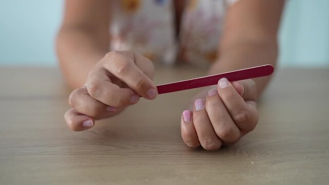 Close up of a woman filing her fingernails with a nail file during a DIY manicure at home. Natural nail care, beauty routine and personal grooming.