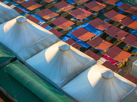 Aerial view of a market featuring large white conical tent roofs and rows of red-roofed stalls under bright sunlight in Belgrade, City of Belgrade, Serbia.