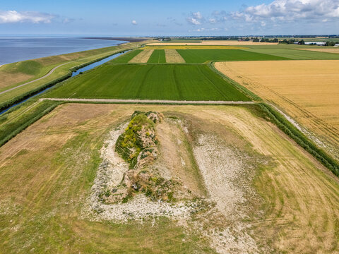 Aerial view of the Dijk van een wijf sculpture in a rural landscape with agricultural fields, a dike, and the Wadden Sea in the distance in Oosterbierum, Friesland, Netherlands.