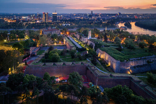 Aerial view of Belgrade Fortress surrounded by historic stone walls, lush greenery, and the confluence of the Sava and Danube rivers at sunset in Belgrade, City of Belgrade, Serbia.