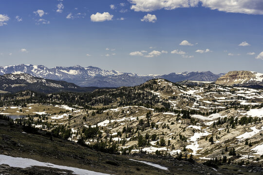 Aerial view of Beartooth Pass featuring rugged mountain terrain with patches of snow, evergreen trees, and rocky slopes in Park County, Wyoming, United States.