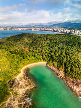 Aerial view of Praia do Ermitao featuring a secluded beach with turquoise water, surrounded by lush green hills and rocky cliffs, with a distant skyline, Guarapari, Espirito Santo, Brazil.