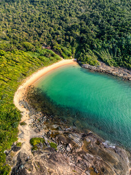 Aerial view of Praia do Ermitao, a secluded beach with turquoise waters, golden sand, and lush green forest surroundings in Guarapari, Espirito Santo, Brazil.