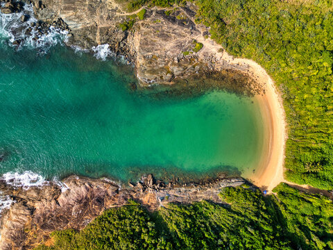 Aerial view of Praia do Ermitao with turquoise water, rocky cliffs, and dense green vegetation in Guarapari, Espirito Santo, Brazil.