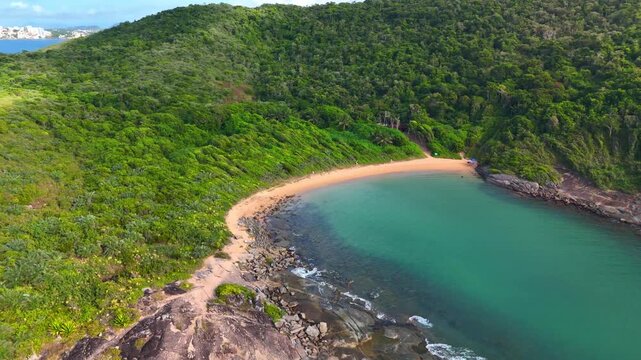Aerial view of the secluded Praia do Ermitao beach with turquoise waters and lush green forest surrounding the coastline in Guarapari, Espirito Santo, Brazil.