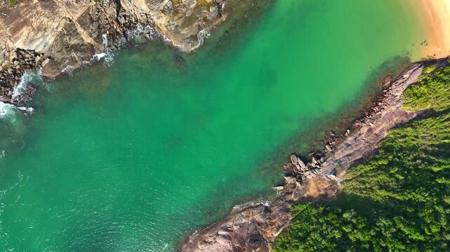 Aerial view of Praia do Ermitao with turquoise waters, rocky coastline, and lush green forest in Guarapari, Espirito Santo, Brazil.
