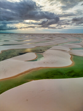 Aerial view of Lagoa Bonita featuring white sand dunes and vibrant green rainwater lagoons under a dramatic cloudy sky in Barreirinhas, State of Maranhao, Brazil.