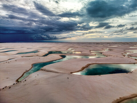 Aerial view of Lagoa Bonita with turquoise lagoons nestled among vast white sand dunes under a dramatic stormy sky in Barreirinhas, State of Maranhao, Brazil.