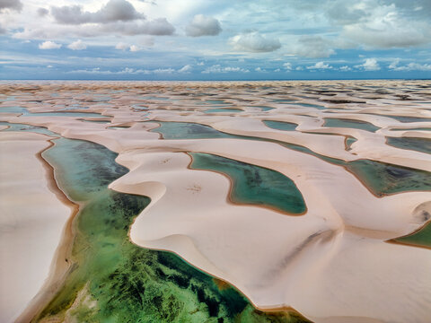 Aerial view of Lagoa Bonita featuring white sand dunes and turquoise lagoons under a cloudy sky in Barreirinhas, Maranhao, Brazil.