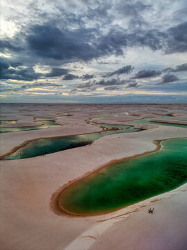 Aerial view of Lagoa Bonita in Lencois Maranhenses National Park, featuring white sand dunes and turquoise lagoons under a dramatic cloudy sky in Barreirinhas, State of Maranhao, Brazil.