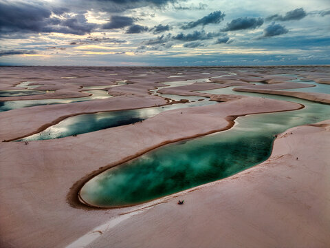 Aerial view of Lagoa Bonita featuring turquoise lagoons nestled among white sand dunes under a dramatic cloudy sky in Barreirinhas, State of Maranhao, Brazil.