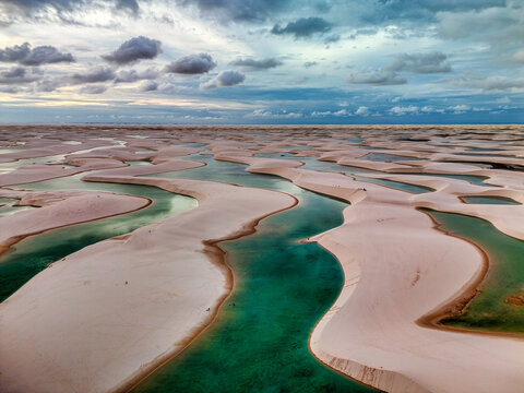 Aerial view of Lagoa Bonita with white sand dunes and turquoise lagoons under a cloudy sky in Barreirinhas, State of Maranhao, Brazil.