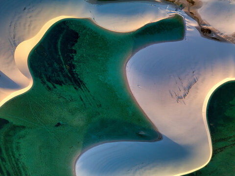 Aerial view of Parque Nacional dos Lencois Maranhenses featuring white sand dunes and turquoise lagoons under soft light in MA, Brazil.