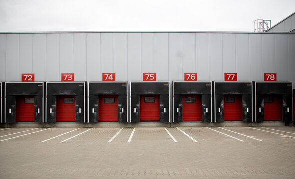 View of a modern industrial warehouse exterior featuring multiple red loading dock doors numbered 72 through 78 under a grey metal facade in Vilnius, Vilnius County, Lithuania.
