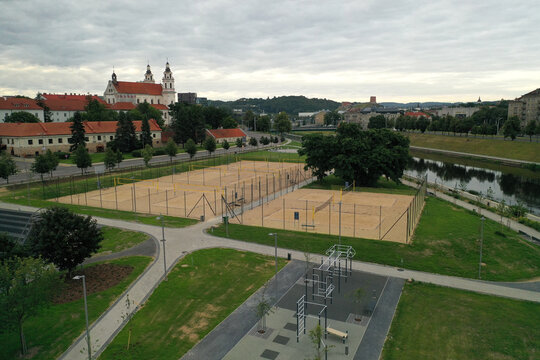 Aerial view of sand volleyball courts and a fitness area near the Neris River with the Church of St. Philip and St. James in the background in Lithuania.