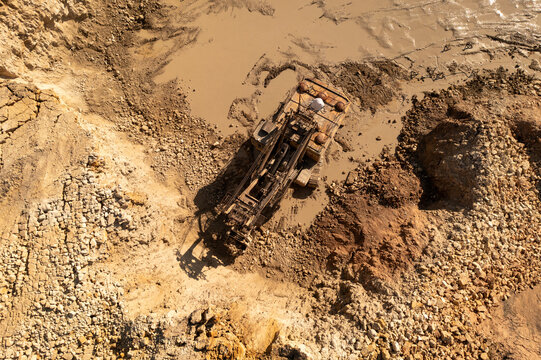Aerial view of a heavy industrial drilling machine operating in a muddy limestone quarry with textured rock formations and wet earth in Naujoji Akmene, Siauliai County, Lithuania.