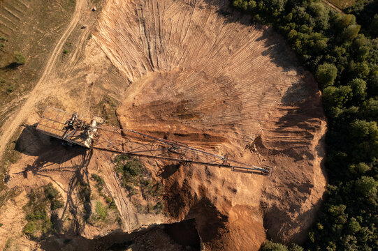 Aerial view of a large dragline excavator operating in an open-pit quarry with exposed soil and surrounding forest in Naujoji Akmene, Siauliai County, Lithuania.