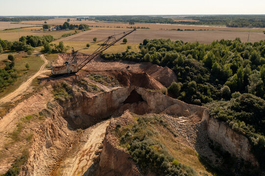 Aerial view of an industrial quarry with a large dragline excavator, deep excavation pits, and surrounding forest in Naujoji Akmene, Siauliai County, Lithuania.