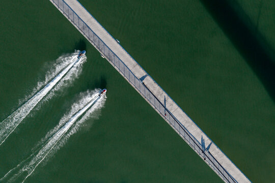 Aerial view of a bridge over the Sava River with two jet skis creating white wakes in the water in Sremska Mitrovica, Vojvodina, Serbia.