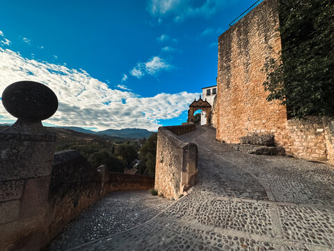 View of the historic stone archway and cobblestone path leading through the ancient walls of Ronda, Andalusia, Spain.