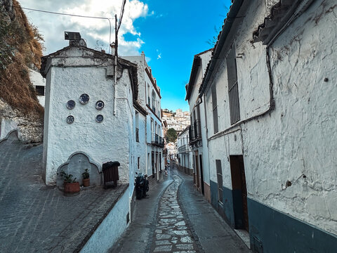 Setenil de las Bodegas, Andalusia, Spain - 27 October 2025: View of a narrow cobblestone street lined with white-washed houses, decorative wall plates, and a clear blue sky.