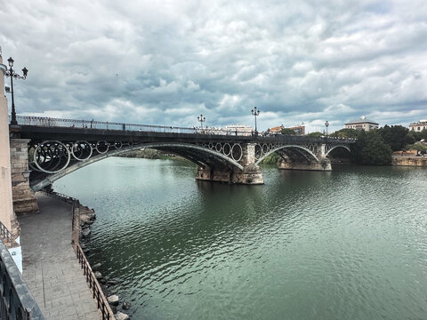 Seville, Spain - 01 November 2025: View of the historic Puente de Isabel II bridge spanning the Guadalquivir River under a cloudy sky in Seville, Spain.