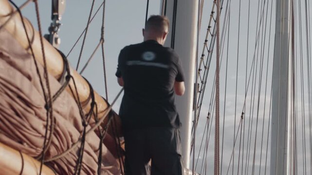 Sailor works on the big expeditional sailing vessel moving in the open ocean