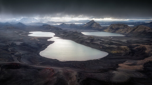 Aerial view of Fjallabak Nature Reserve featuring volcanic lakes surrounded by dark basaltic terrain and rugged mountains under a dramatic stormy sky in Rangarthing ytra, Iceland.