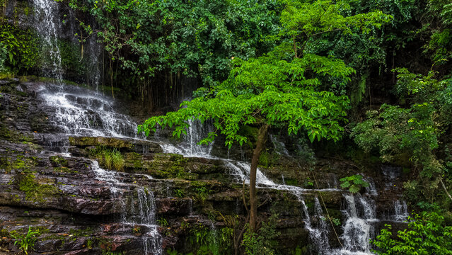 Aerial view of Oboadaka Falls with water cascading over tiered dark rocks surrounded by lush tropical vegetation and dense forest canopy in Aburi, Eastern Region, Ghana.