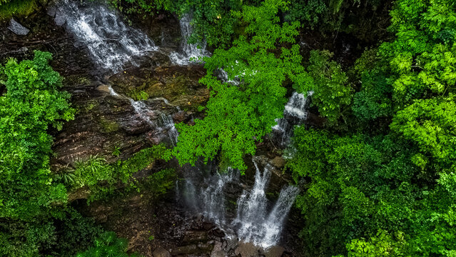 Aerial view of Oboadaka Falls cascading over rocky cliffs surrounded by lush green tropical forest in Aburi, Eastern Region, Ghana.