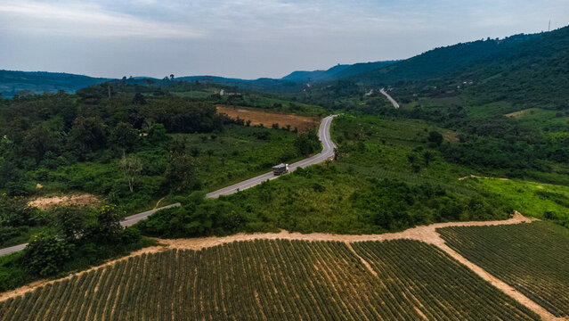 Aerial view of a winding road through the lush landscape of Pokrom with a truck driving along the asphalt, surrounded by agricultural fields and rolling hills in Aburi, Eastern Region, Ghana.